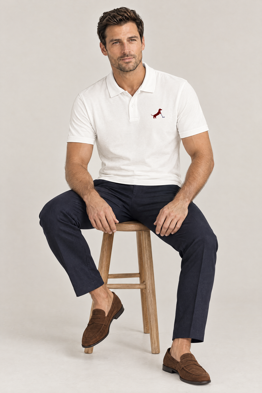 Man sitting on a wooden stool in white Putting dachshund golf polo and navy trousers. Color: White