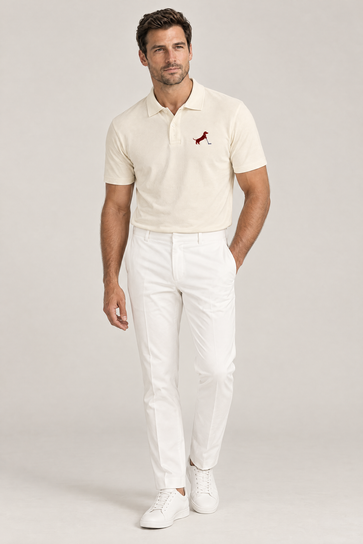 Man standing relaxed with one hand in his pocket wearing apricot Putting dachshund golf polo and white trousers, full-body studio look. Color: Apricot