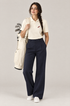 Woman carrying a golf bag in apricot Putting dachshund golf polo and navy wide-leg trousers, full-body studio look. Color: Apricot