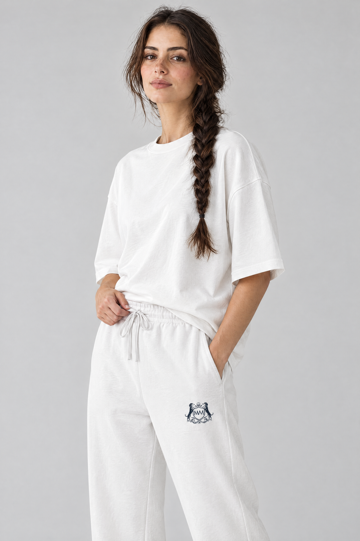 Woman in white Club Crest sweatpants, three-quarter view with a hand on the drawstring waistband
