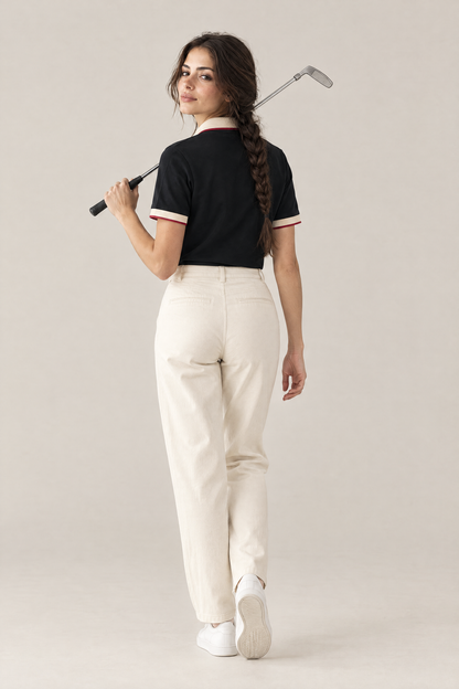 Woman walking away with a putter over her shoulder in the black Club Crest polo and cream trousers. Color: Black with Apricot