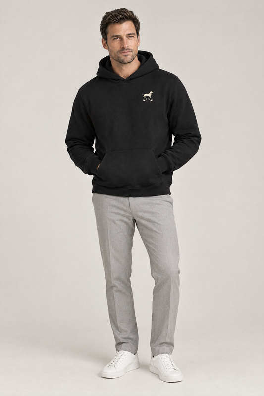 Man standing relaxed with hands in the pocket of a black Club & Swing dachshund golf hoodie and light grey trousers, full-body studio look. Color: Black