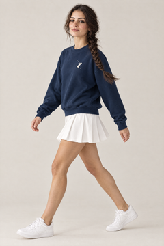 Woman walking in side view in navy Swing dachshund golf sweatshirt and white pleated tennis skirt. Color: Navy