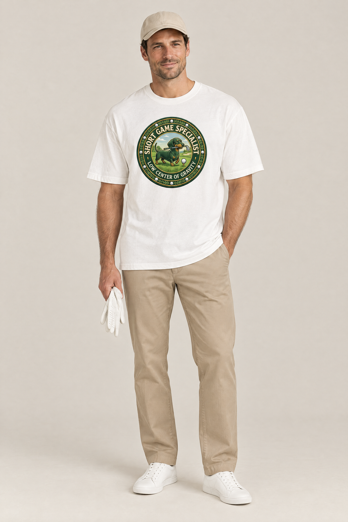 Man wearing the Short Game Crest Dachshund Golf Tee in white with khaki trousers and a beige cap. Color: White