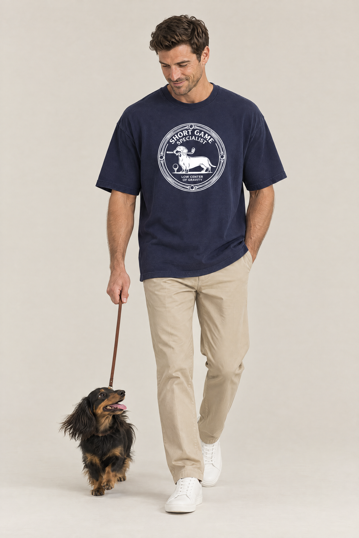 Man walking a long-haired dachshund on a leash in the navy Short Game Specialist Dachshund Golf Tee. Color: Navy