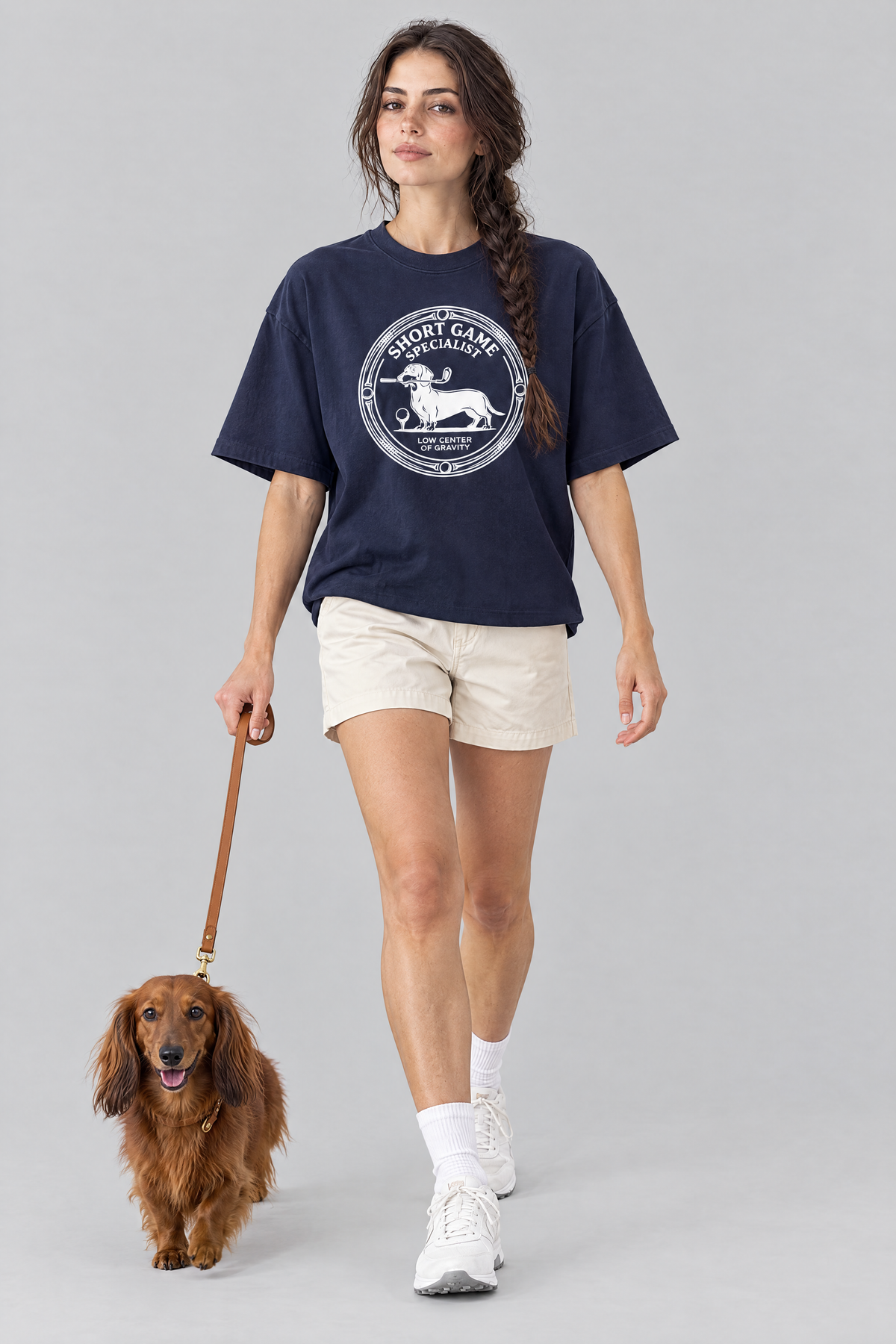 Woman walking a long-haired dachshund on a leash in the navy Short Game Specialist Dachshund Golf Tee. Color: Navy