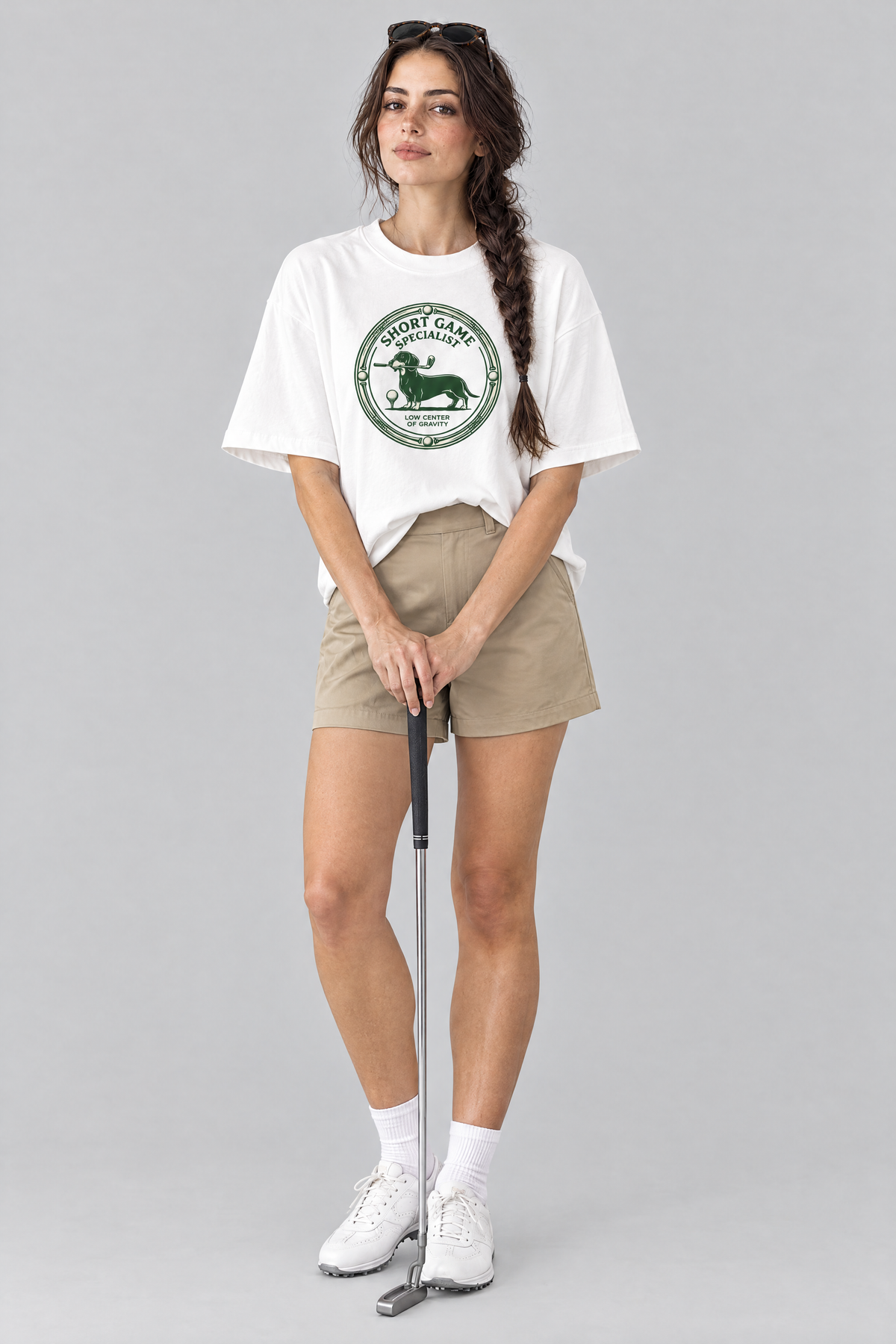 Woman wearing the Short Game Specialist Dachshund Golf Tee in white with khaki golf shorts, holding a putter. Color: White