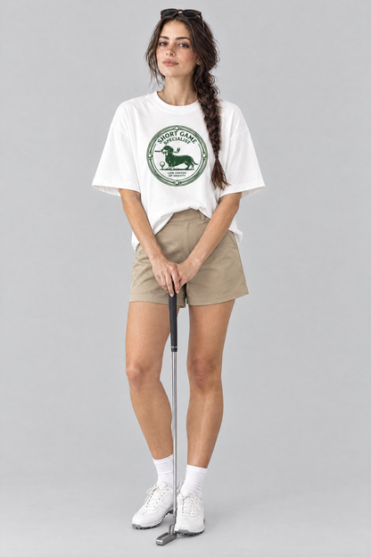 Woman wearing the Short Game Specialist Dachshund Golf Tee in white with khaki golf shorts, holding a putter. Color: White