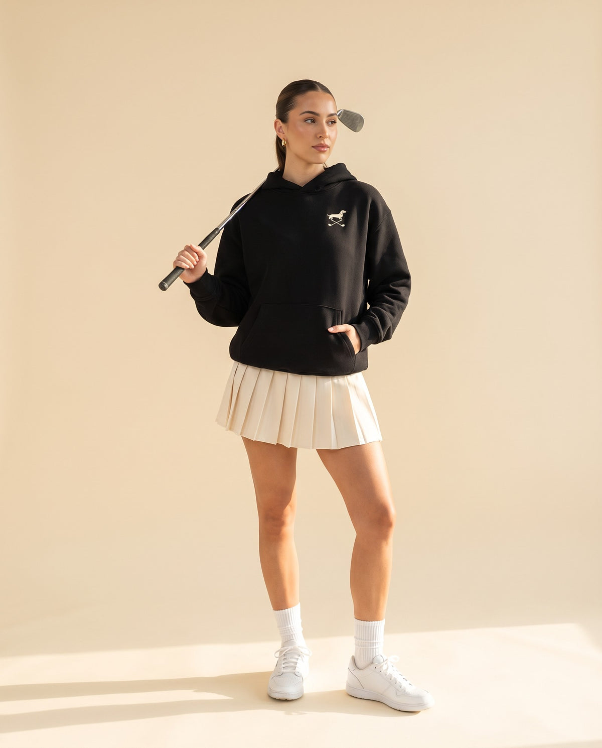 Woman wearing Club & Swing dachshund golf hoodie, full-body studio look. Color: Black