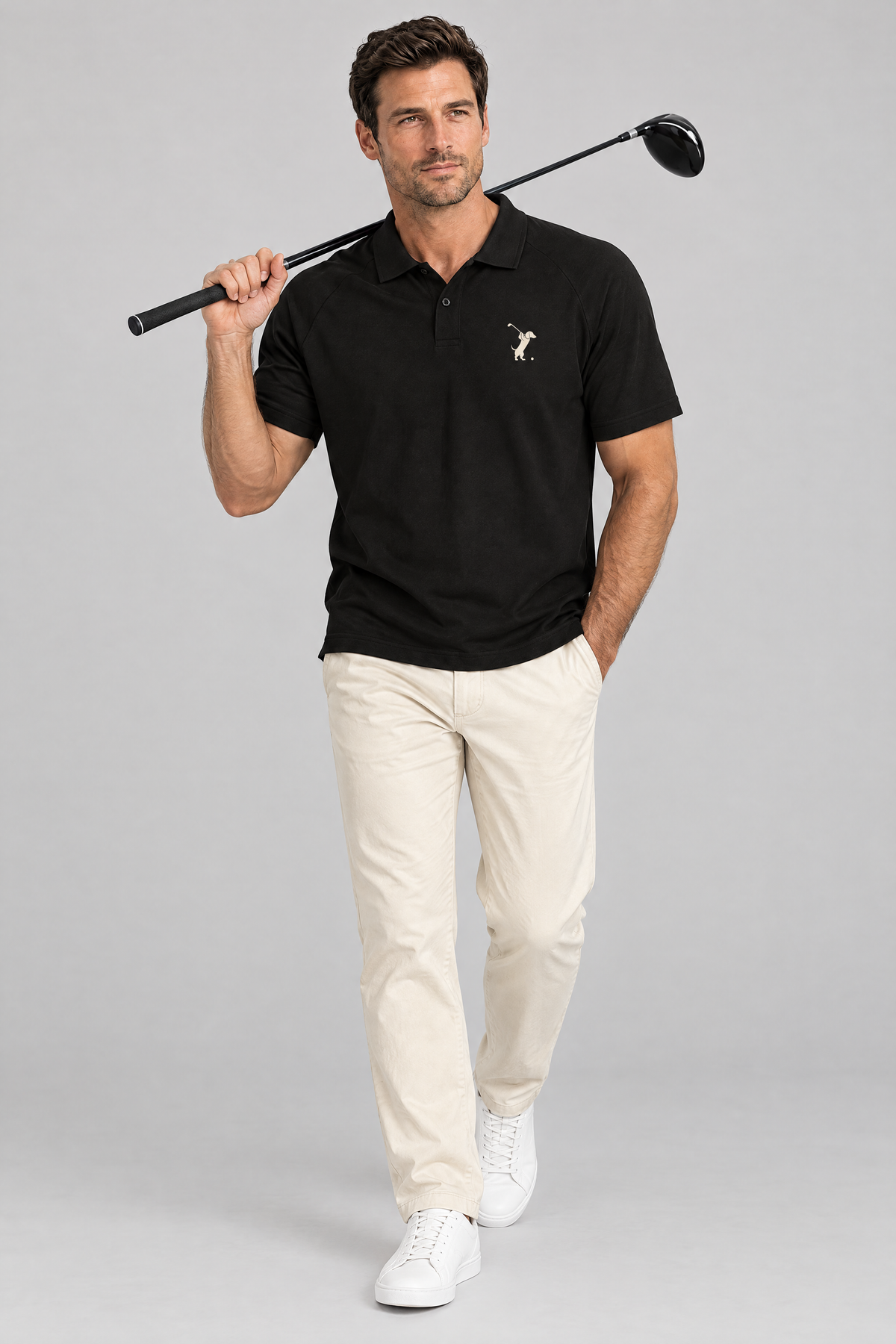 Man walking with a driver on his shoulder in the black Swing dachshund golf polo and cream chinos. Color: Black