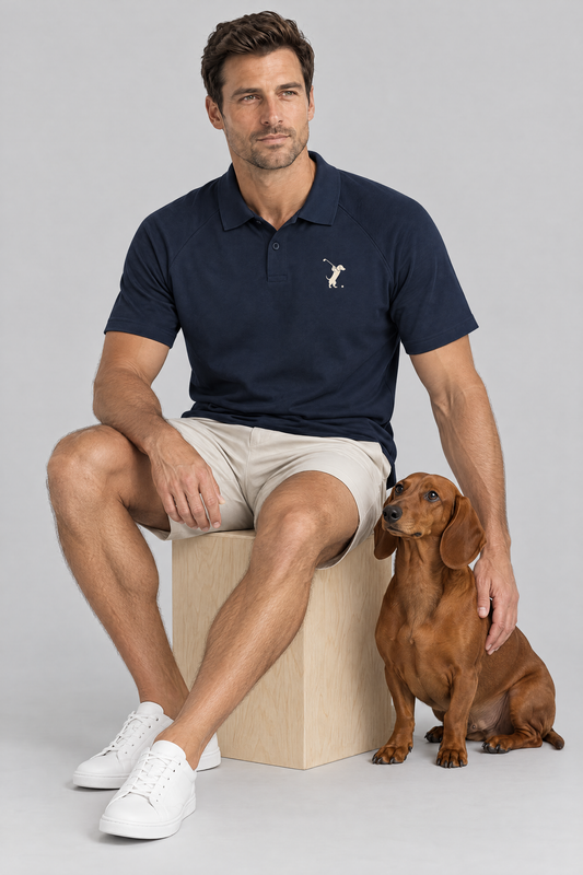 Man sitting on a wooden box with a red dachshund in the navy blue Swing dachshund golf polo and stone golf shorts. Color: Navy Blue