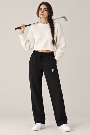 Woman holding a putter over her shoulder in black Swing dachshund golf sweatpants with the small cream dachshund golfer on the thigh and a white cropped sweater. Color: Black