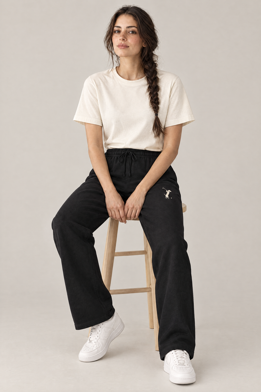 Woman sitting on a wooden stool in black Swing dachshund golf sweatpants and a cream tee. Color: Black