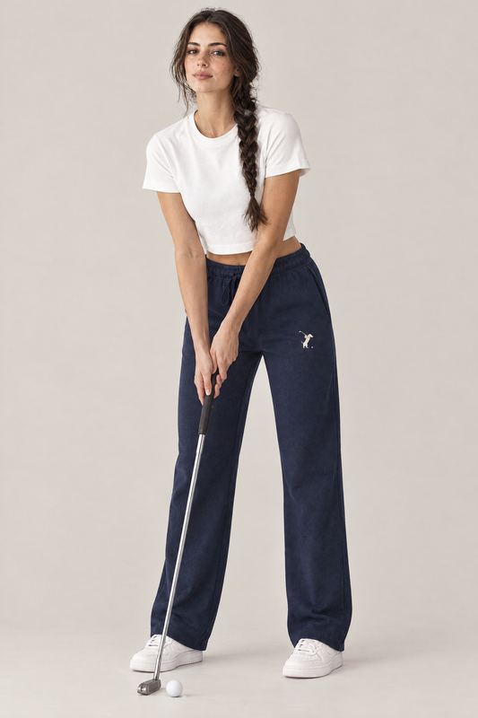 Woman in a relaxed putting stance with a putter in navy blue Swing dachshund golf sweatpants with the small cream dachshund golfer on the thigh and a white cropped tee. Color: Navy Blue