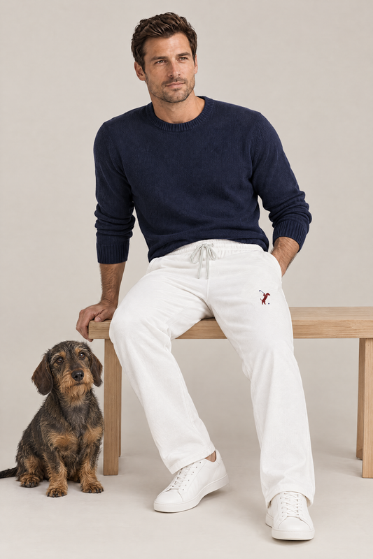 Man sitting on a wooden bench with a wire-haired dachshund in white Swing dachshund golf sweatpants with the small burgundy dachshund golfer on the thigh and a navy knit sweater. Color: White