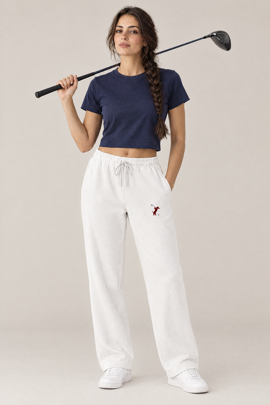 Woman holding a driver over her shoulder in white Swing dachshund golf sweatpants with the small burgundy dachshund golfer on the thigh and a navy cropped tee. Color: White