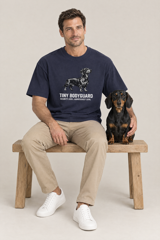 Man sitting on a wooden bench next to a black and tan dachshund in the navy Tiny Bodyguard Dachshund Tee. Color: Navy