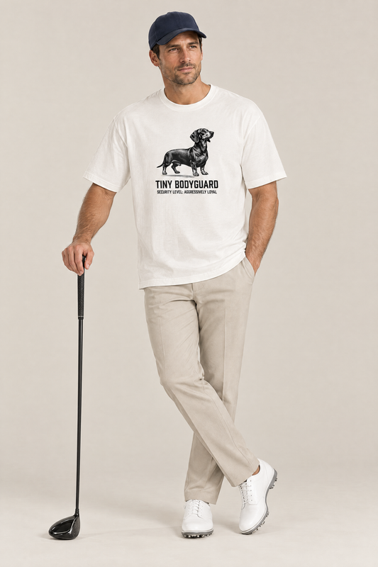 Man in a navy cap leaning on a golf driver in the white Tiny Bodyguard Dachshund Tee. Color: White