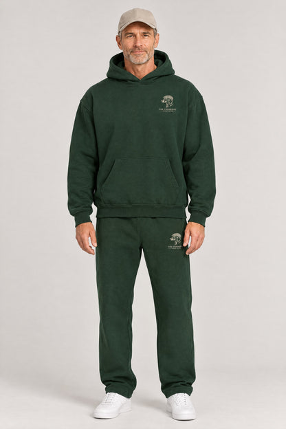 Man wearing The Long Drive dachshund golf hoodie and matching Underdog Golf Club sweatpants in Blackish Green, front view. Color: Blackish Green