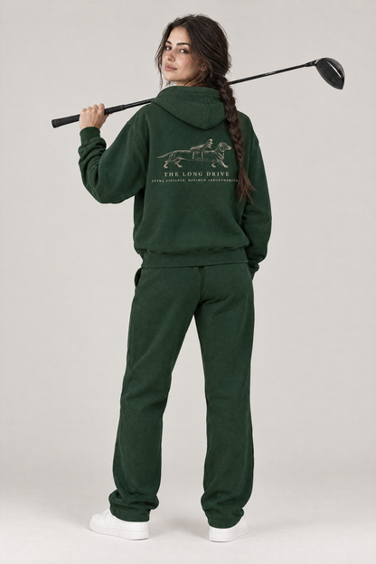Woman with a driver over her shoulder, back view of The Long Drive dachshund golf hoodie in Blackish Green with the large back print. Color: Blackish Green