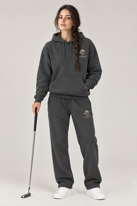 Woman holding a putter in The Long Drive dachshund golf hoodie and matching Underdog Golf Club sweatpants in Dark Gray, front view. Color: Dark Gray