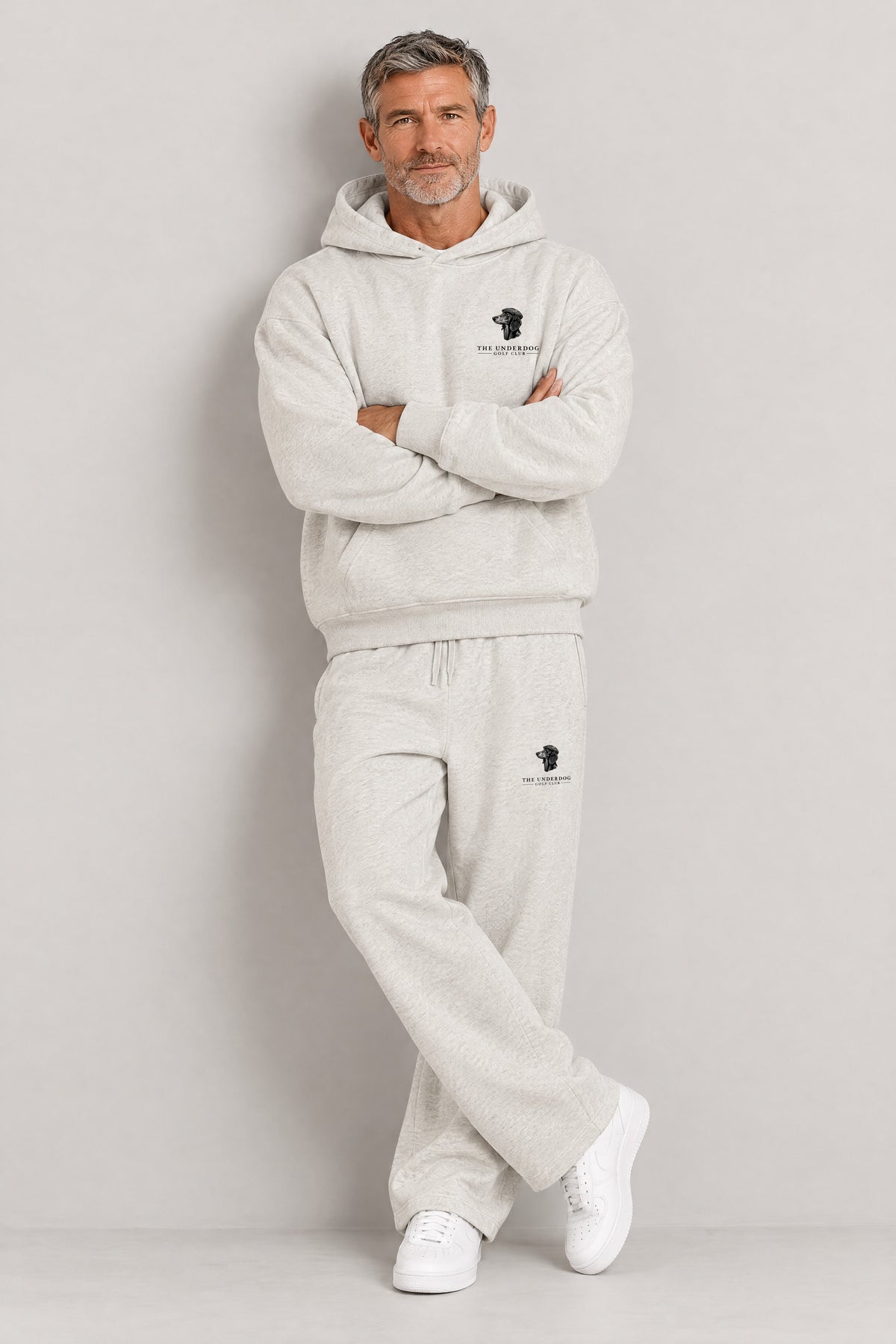 Man seated in The Long Drive dachshund golf hoodie and sweatpants in Oat Gray. Color: Oat Gray
