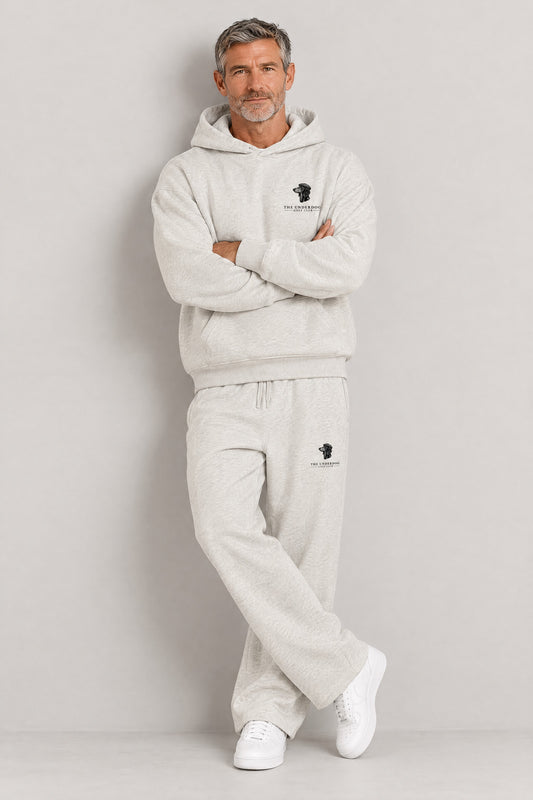 Man seated in The Long Drive dachshund golf hoodie and sweatpants in Oat Gray. Color: Oat Gray