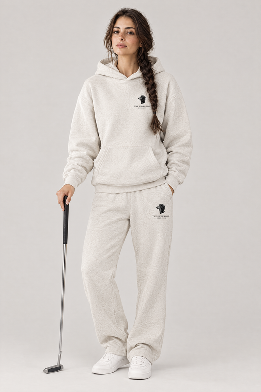 Woman holding a putter in The Long Drive dachshund golf hoodie and matching Underdog Golf Club sweatpants in Oat Gray, front view. Color: Oat Gray