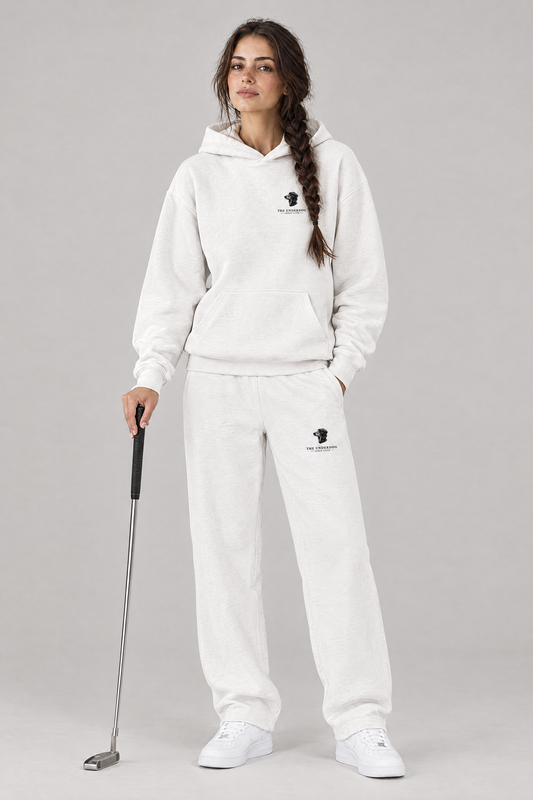 Woman holding a putter in The Long Drive dachshund golf hoodie and matching Underdog Golf Club sweatpants in White, front view. Color: White