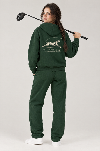 Woman with a driver over her shoulder, back view of The Sweet Spot Dalmatian golf hoodie in Blackish Green with the large back print. Color: Blackish Green