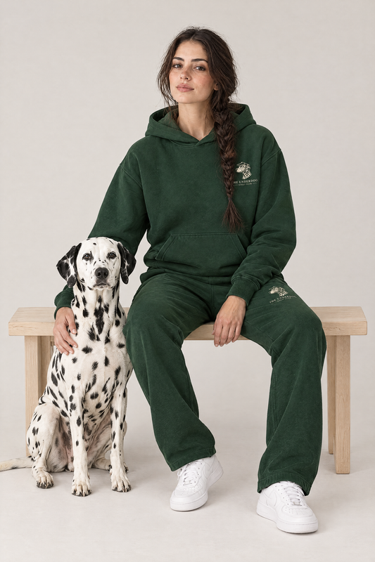 Woman sitting on a wooden bench with a Dalmatian in The Sweet Spot Dalmatian golf hoodie and sweatpants in Blackish Green. Color: Blackish Green
