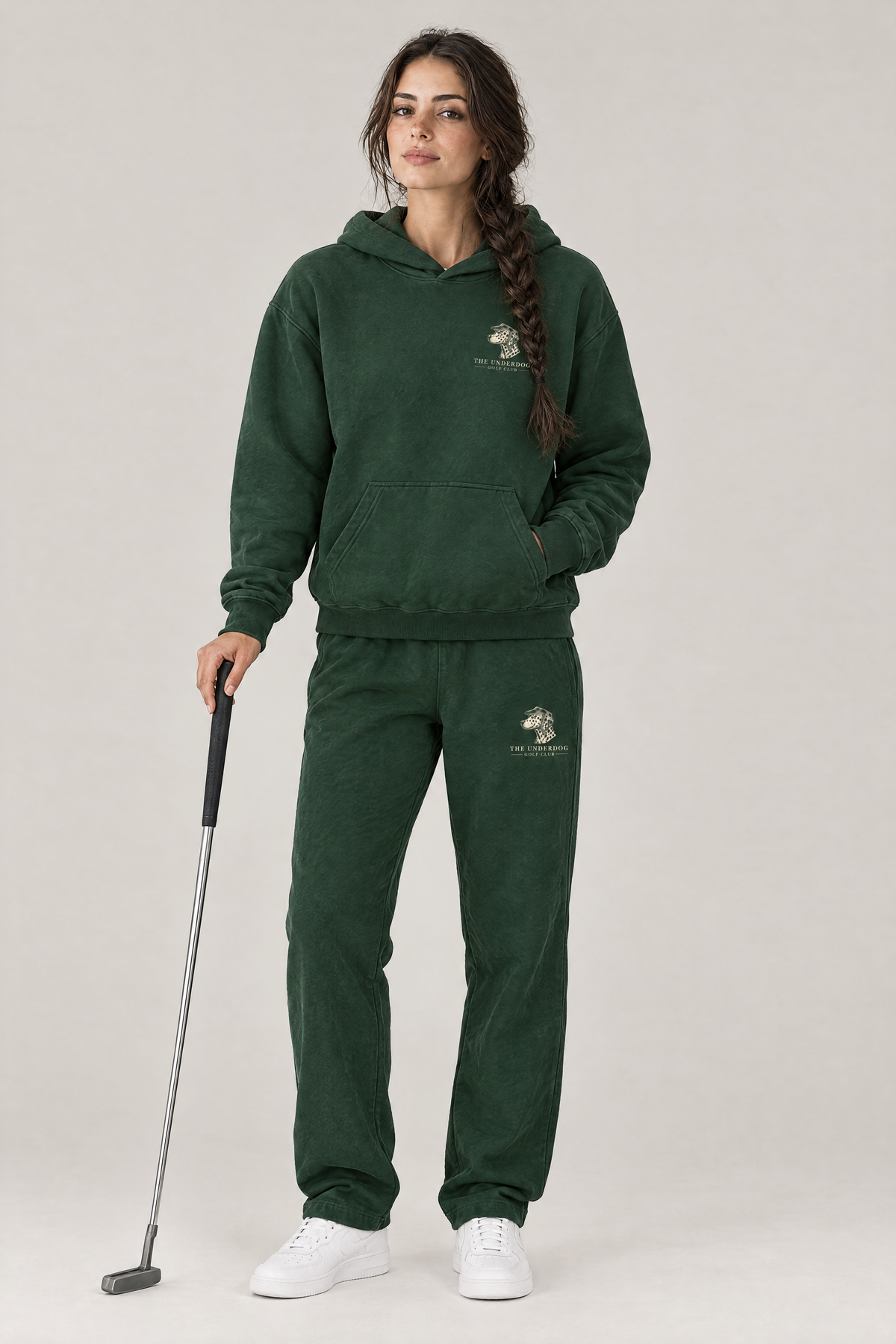 Woman holding a putter in The Sweet Spot Dalmatian golf hoodie and matching Underdog Golf Club sweatpants in Blackish Green, front view. Color: Blackish Green