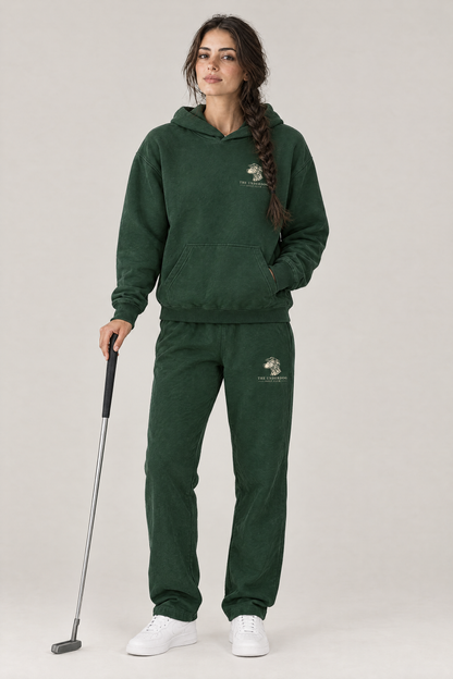 Woman holding a putter in The Sweet Spot Dalmatian golf hoodie and matching Underdog Golf Club sweatpants in Blackish Green, front view. Color: Blackish Green