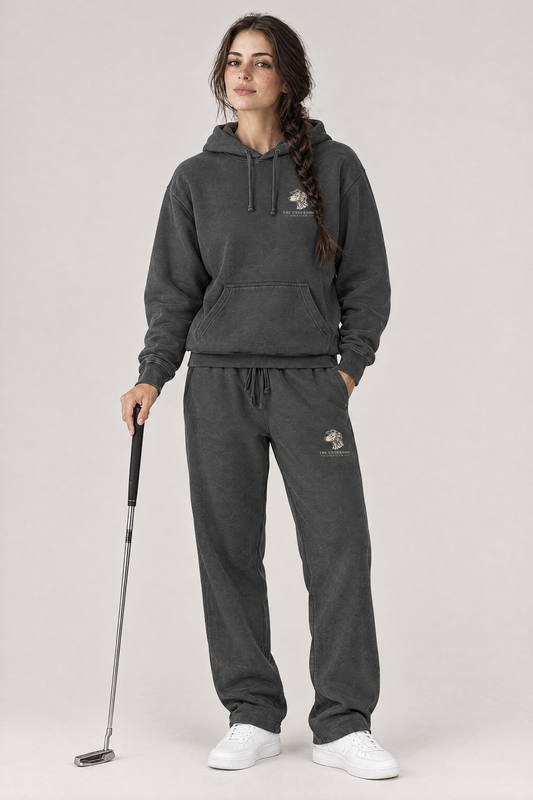 Woman holding a putter in The Sweet Spot Dalmatian golf hoodie and matching Underdog Golf Club sweatpants in Dark Gray, front view. Color: Dark Gray