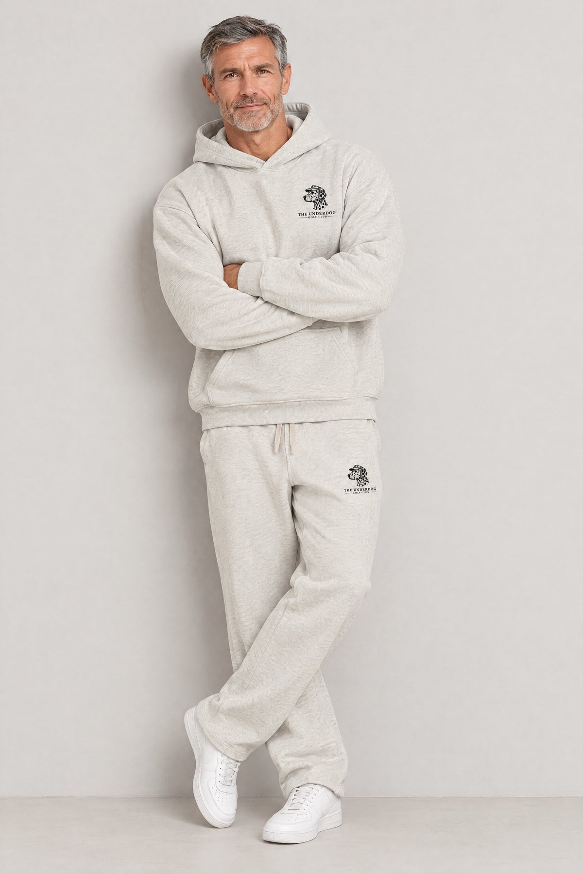 Man seated in The Sweet Spot Dalmatian golf hoodie and sweatpants in Oat Gray. Color: Oat Gray