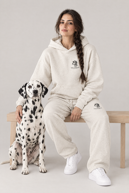 Woman sitting on a wooden bench with a Dalmatian in The Sweet Spot Dalmatian golf hoodie and sweatpants in Oat Gray. Color: Oat Gray