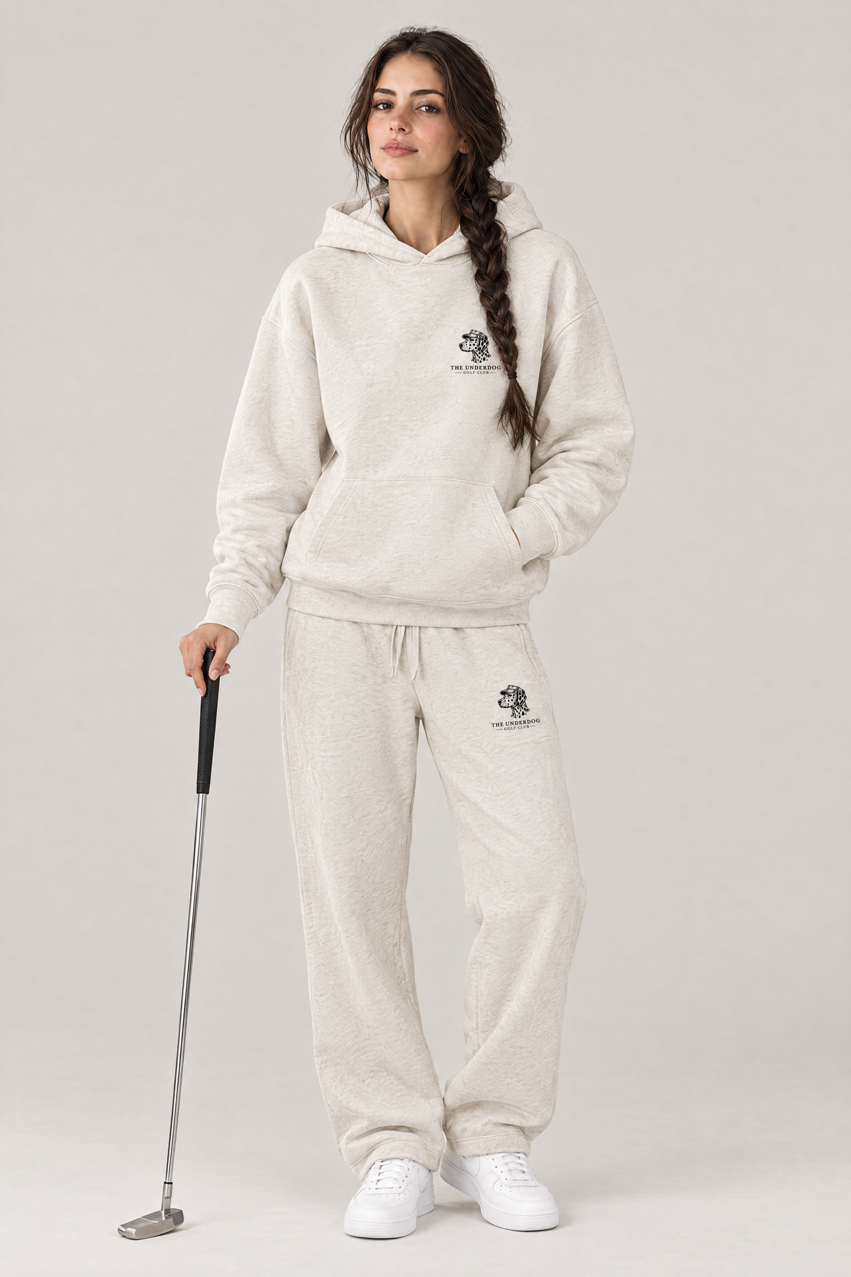 Woman holding a putter in The Sweet Spot Dalmatian golf hoodie and matching Underdog Golf Club sweatpants in Oat Gray, front view. Color: Oat Gray