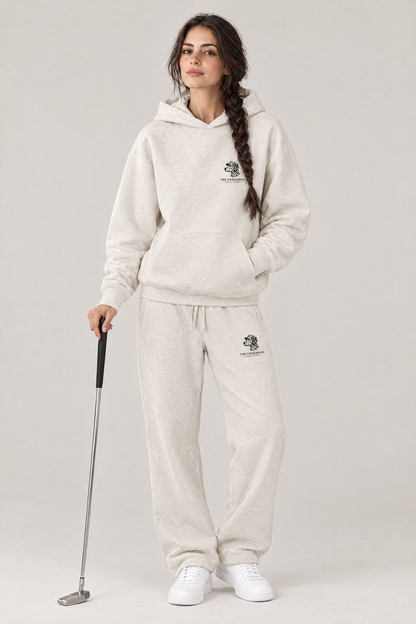 Woman holding a putter in The Sweet Spot Dalmatian golf hoodie and matching Underdog Golf Club sweatpants in Oat Gray, front view. Color: Oat Gray