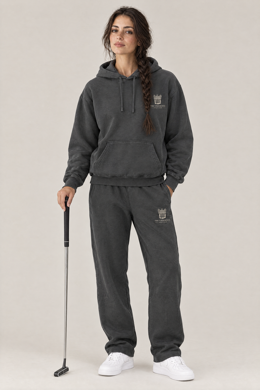 Woman holding a putter in The Marshal French Bulldog golf hoodie and matching Underdog Golf Club sweatpants in Dark Gray, front view. Color: Dark Gray
