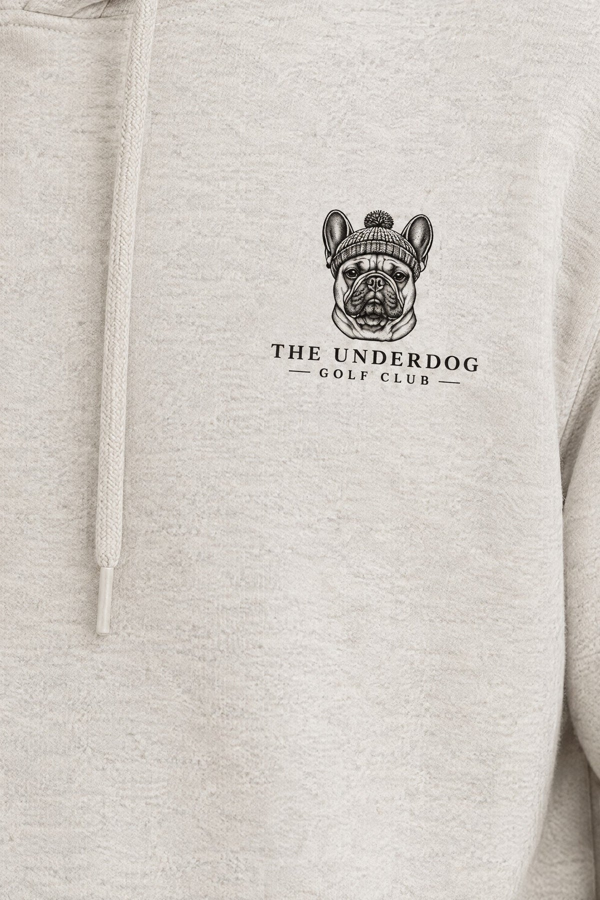 Close-up of The Underdog Golf Club French Bulldog crest printed on the left chest of the Oat Gray hoodie. Color: Oat Gray
