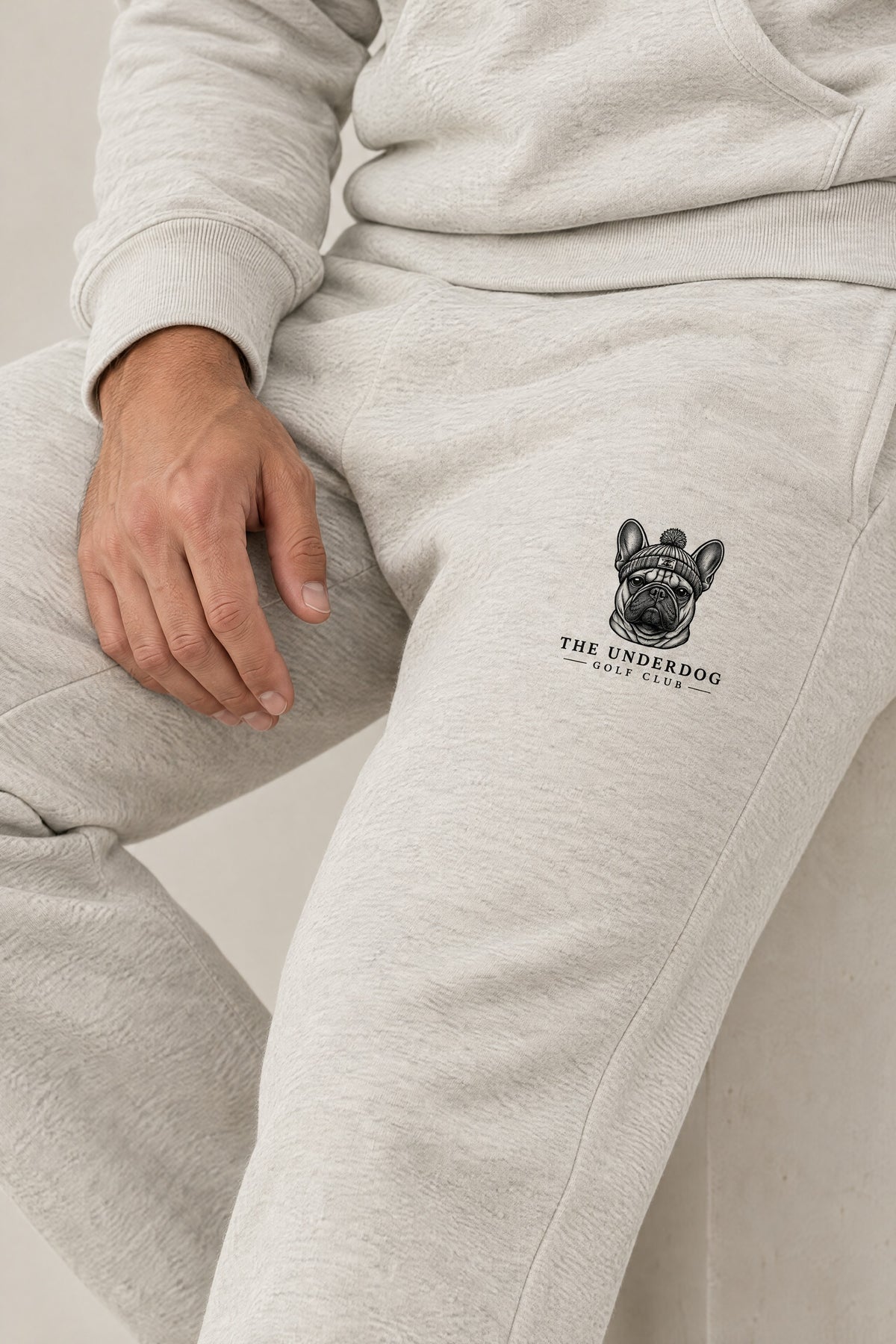 Close-up of The Underdog Golf Club French Bulldog crest on the left thigh of the Oat Gray sweatpants. Color: Oat Gray