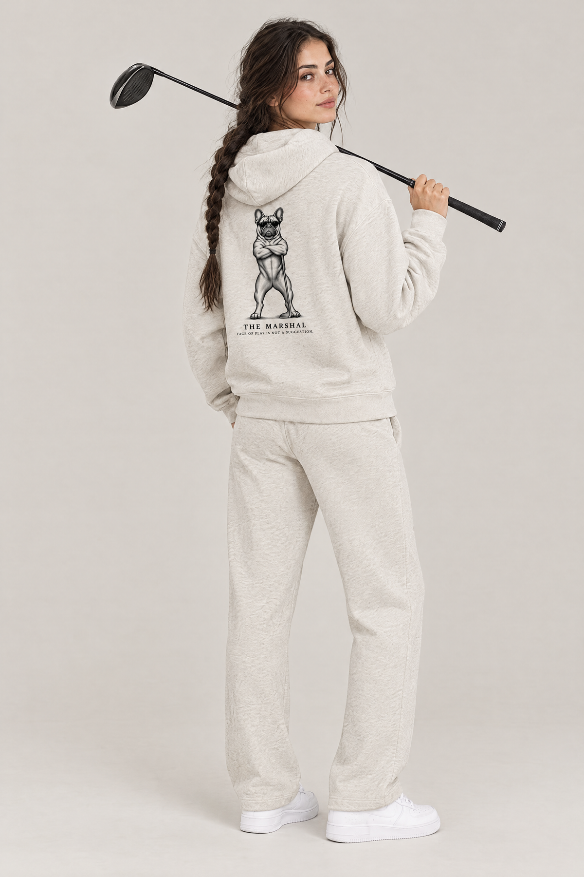 Woman with a driver over her shoulder, back view of The Marshal French Bulldog golf hoodie in Oat Gray with the large back print. Color: Oat Gray