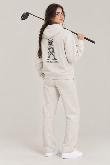 Woman with a driver over her shoulder, back view of The Marshal French Bulldog golf hoodie in Oat Gray with the large back print. Color: Oat Gray