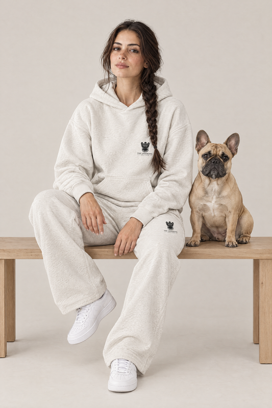 Woman sitting on a wooden bench with a fawn French Bulldog in The Marshal French Bulldog golf hoodie and sweatpants in Oat Gray. Color: Oat Gray