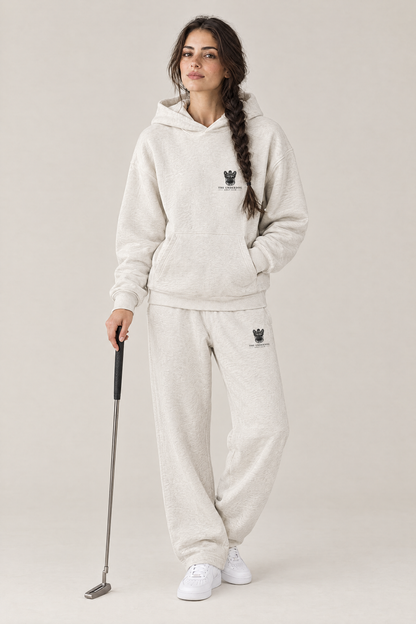 Woman holding a putter in The Marshal French Bulldog golf hoodie and matching Underdog Golf Club sweatpants in Oat Gray, front view. Color: Oat Gray