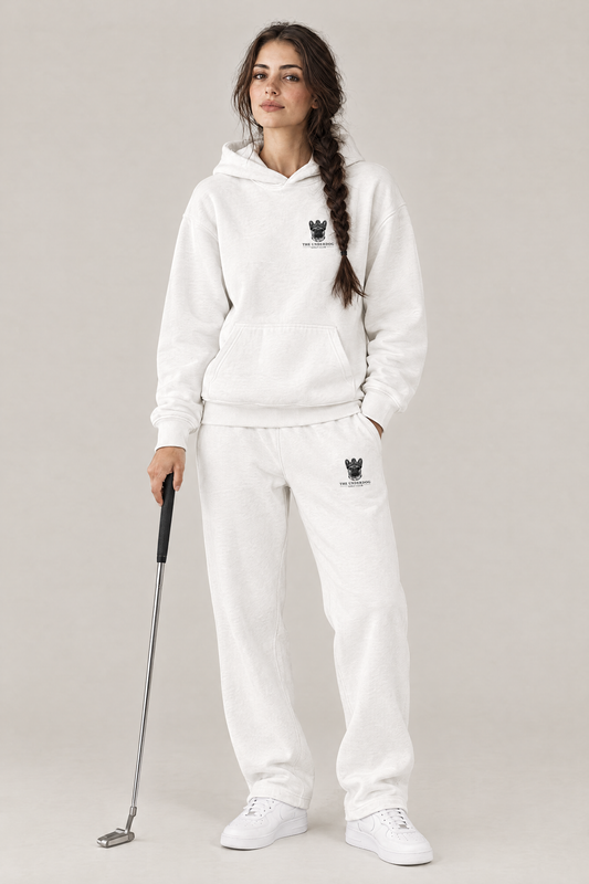 Woman holding a putter in The Marshal French Bulldog golf hoodie and matching Underdog Golf Club sweatpants in White, front view. Color: White