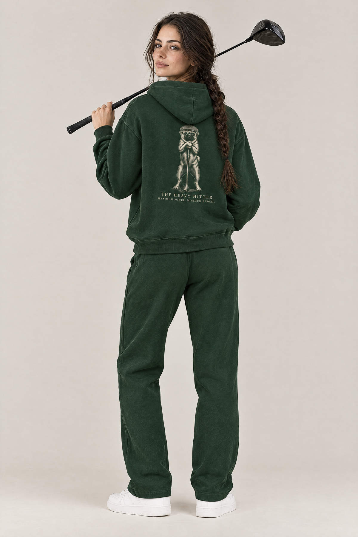 Woman with a driver over her shoulder, back view of The Heavy Hitter pug golf hoodie in Blackish Green with the large back print. Color: Blackish Green