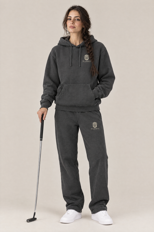 Woman holding a putter in The Heavy Hitter pug golf hoodie and matching Underdog Golf Club sweatpants in Dark Gray, front view. Color: Dark Gray