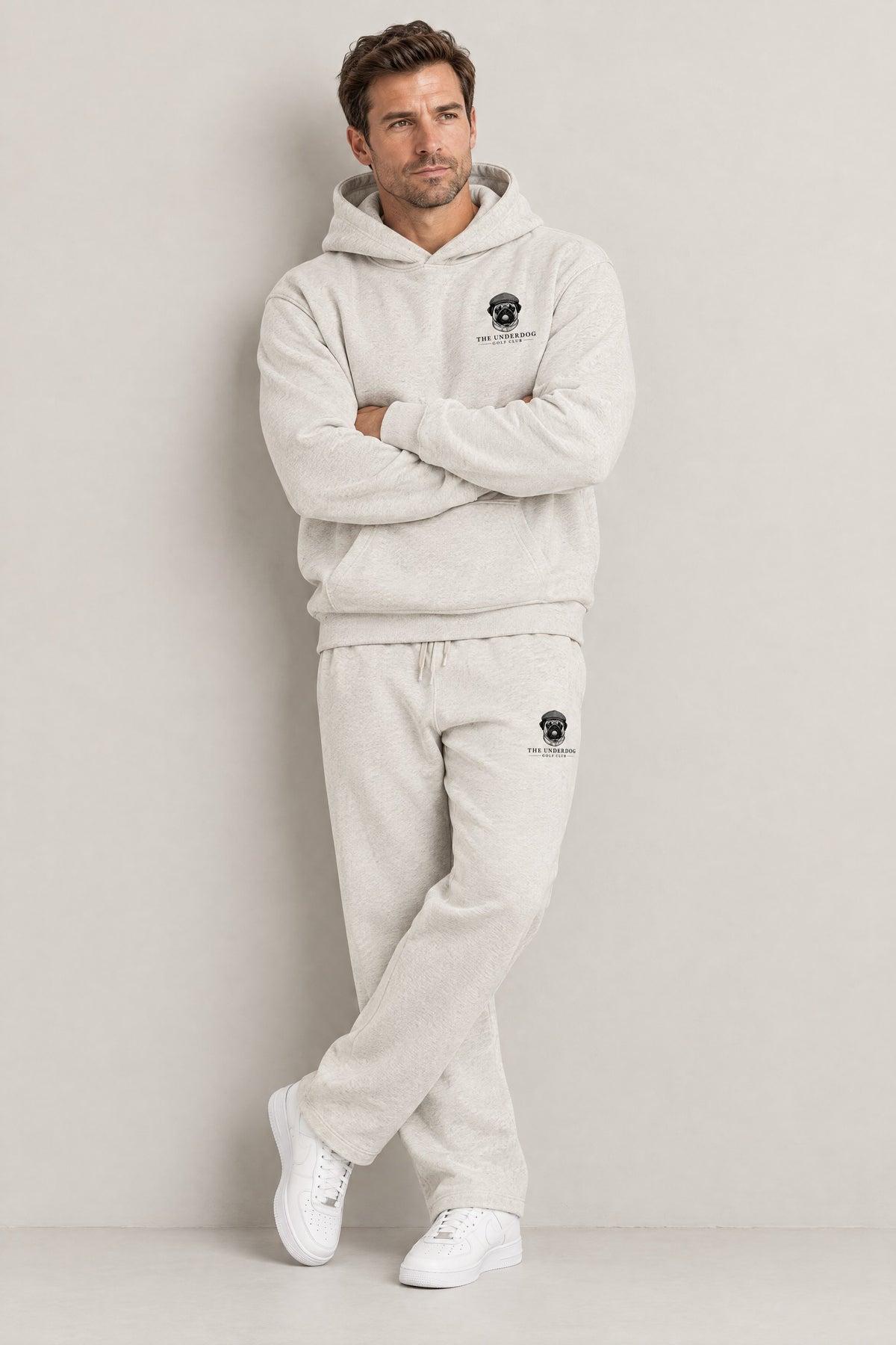 Man seated in The Heavy Hitter pug golf hoodie and sweatpants in Oat Gray. Color: Oat Gray