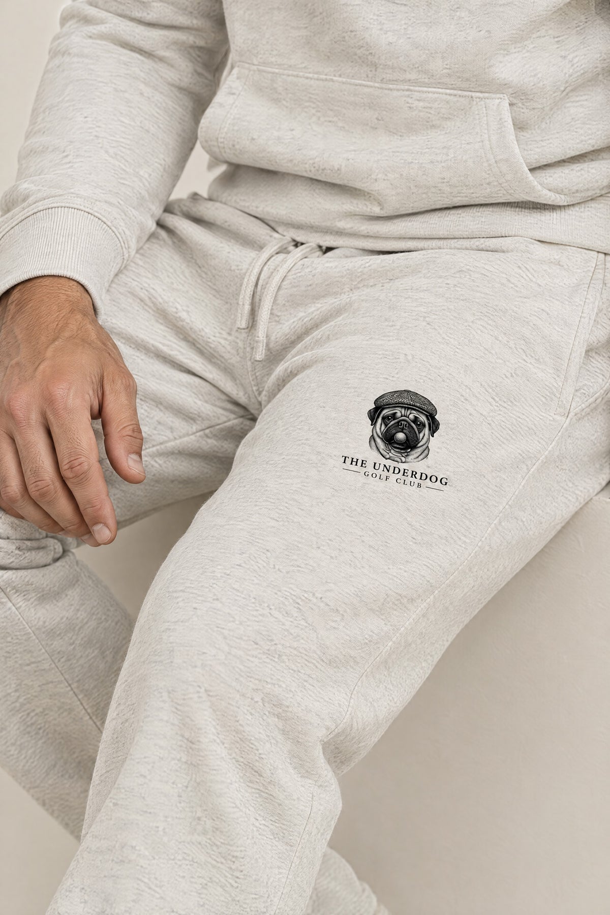 Close-up of The Underdog Golf Club pug crest on the left thigh of the Oat Gray sweatpants. Color: Oat Gray